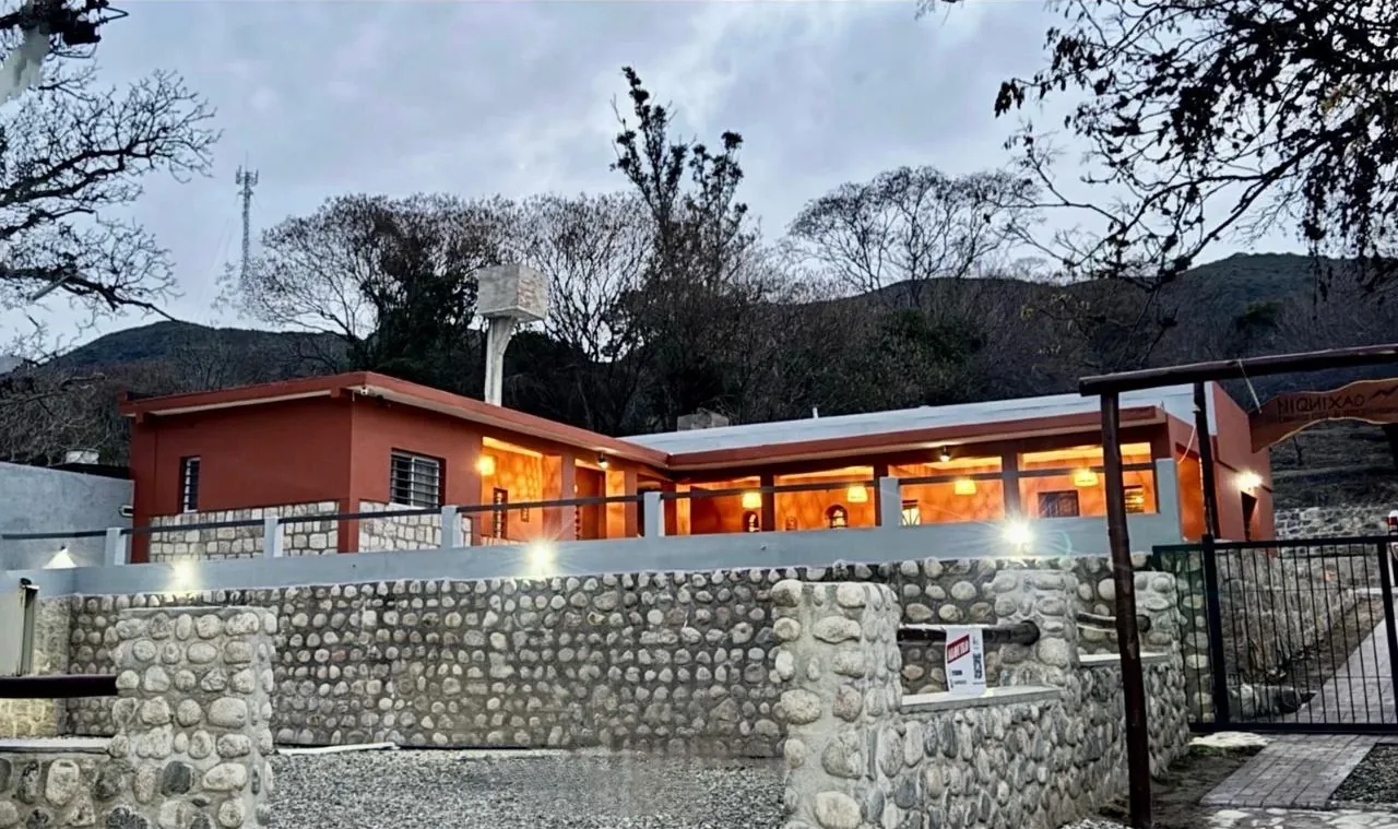 Frente de Alojamiento Niquixao al atardecer, con la galería iluminada y el muro de piedra desde la calle